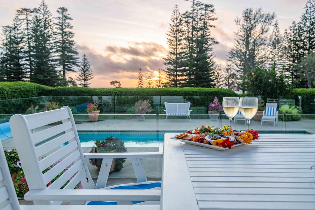 The villa terrace at golden hour, with the pool in the foreground, wine glasses and a charcuterie board on a table, with views stretching out to the horizon.